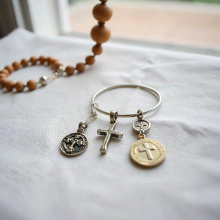 Cross pendant and bracelet with a small saint charm on neutral fabric under soft natural light