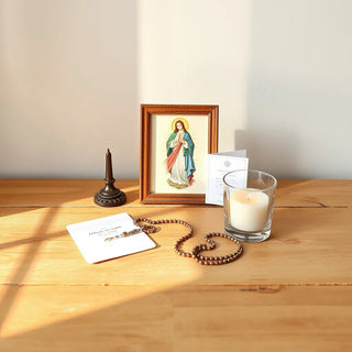 Framed Divine Mercy image, rosary, and prayer card arranged on a wooden table with soft candlelight