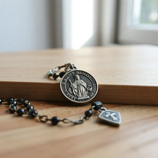 Saint Benedict medal resting on wood with a rosary chain nearby in soft natural light
