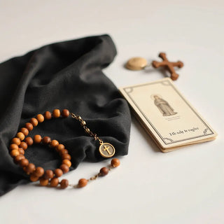 A rosary, saint medal on a chain, and a folded prayer card on a wooden table.