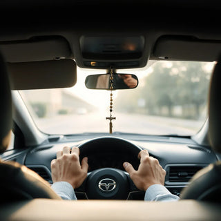 A small devotional hanging near the rearview mirror inside a car with soft daylight and a calm driver