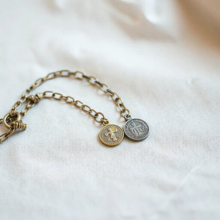 Delicate metal chain with a small religious medal resting on neutral fabric