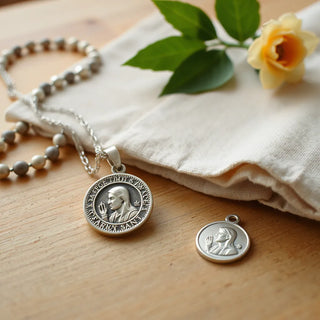 Patron saint medal necklace and bracelet charms resting on a wooden surface with soft warm light