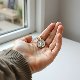Silver miraculous medal on a chain held in a hand under soft natural light