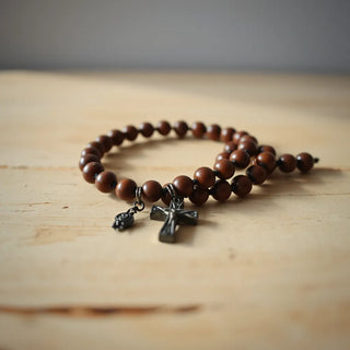 Bead rosary bracelet with a small cross charm lying on a wooden surface in soft daylight