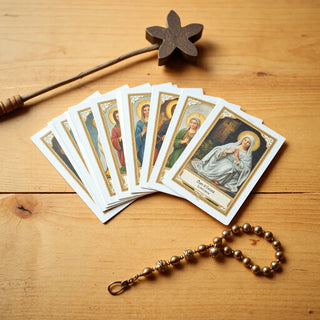 Catholic holy cards fanned on a wooden surface with a rosary nearby