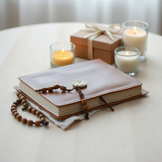 Rosary, prayer book, saint medal, and a small gift box on a light wood table