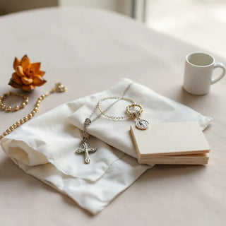 Silver cross necklace, rosary bracelet, and saint charm jewelry arranged on white linen