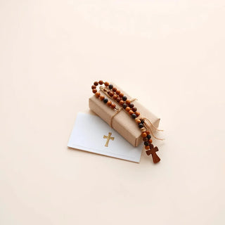 A rosary and a wrapped devotional gift laid on a clean background with soft natural light