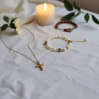 Gold cross necklace and rosary with a charm bracelet on a neutral linen background