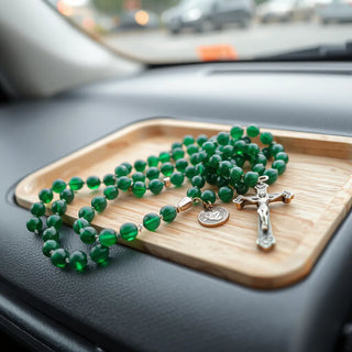 Emerald green rosary beads with a small crucifix resting on a car dashboard tray