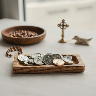 Assorted saint medals on a wooden devotional tray with soft light and a rosary in the background