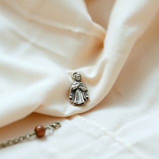 A small saint charm on a delicate chain with subtle rosary beads on a neutral background