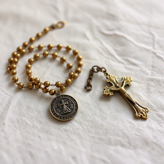Vintage-style rosary, crucifix pendant, and medallion charms with antique patina on neutral fabric