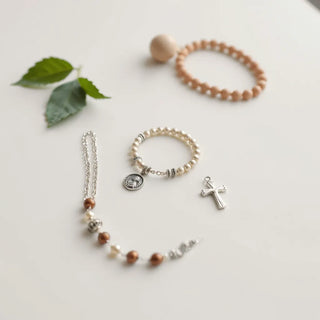 Silver cross pendant, saint medal charm, and beaded devotional bracelet on a light background