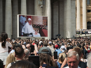 People watch pope francis on a large screen.