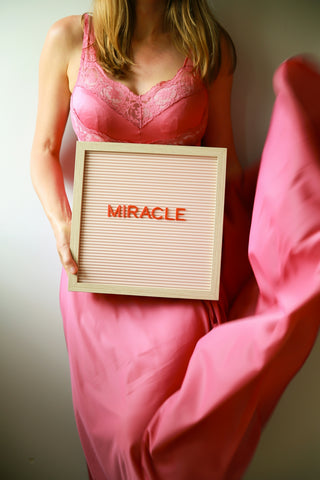 Woman in pink holds sign that says miracle.