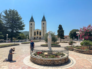 A person kneels before a statue in a church courtyard.