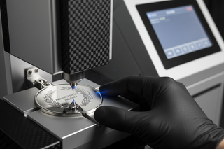 marketing image close-up of a sterling silver medal being engraved by a high-tech engraving machine operated by a human hand